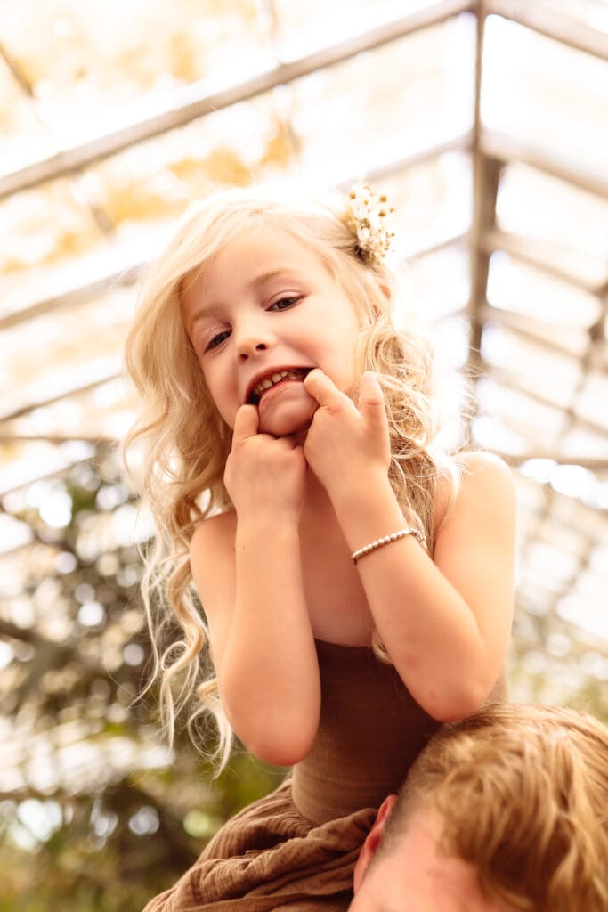 Child sitting on her father's shoulders during an indoor family session near Smithville, MO