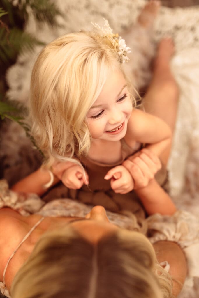 Little girl sharing laughter with her mother during a greenhouse studio family session near Kansas City, MO
