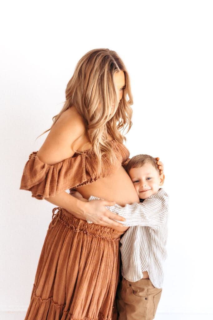 Expecting mother embracing son wearing a dressy maternity outfit during a studio session in Kansas City
