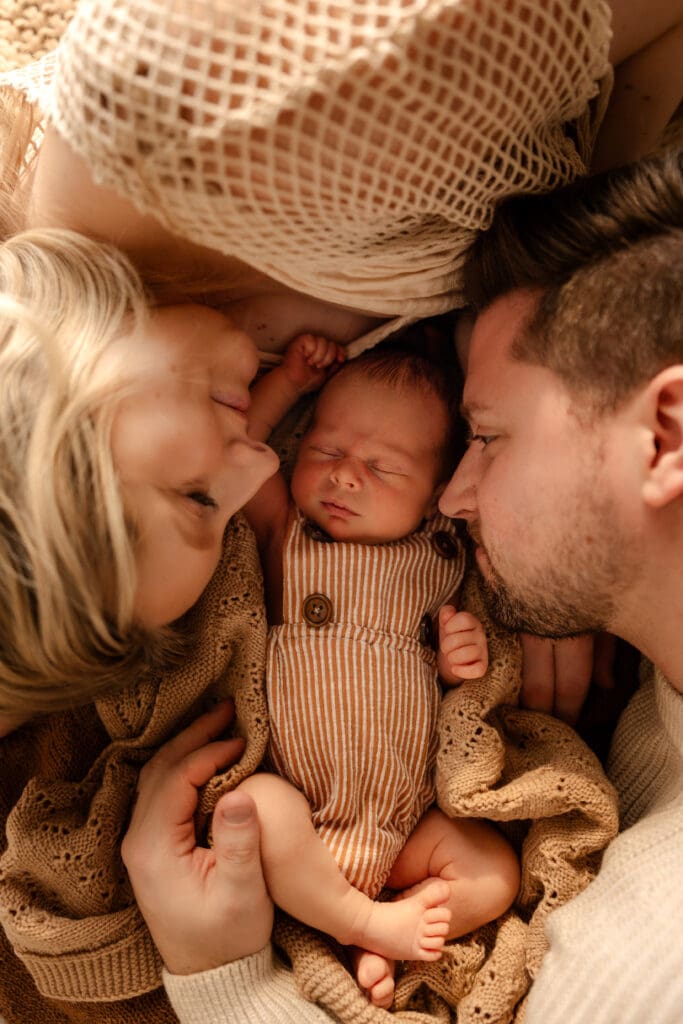 Family newborn session in Kansas City with parents cuddling up to their newborn baby during a relaxed, connection-focused moment.